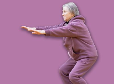 A mature happy woman in a purple tracksuit doing a half squat outdoors. Performs exercises in the autumn park. Full length portrait.