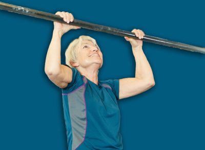 Woman, coach and pull up at gym with support, group and strength training for wellness. Personal trainer, senior client and happy for exercise, calisthenics bar and muscle development at fitness club