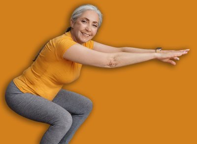 Active senior lady doing squats on domestic workout, training in living room and smiling at camera, copy space. Fit female leading active lifestyle, staying in good shape at home