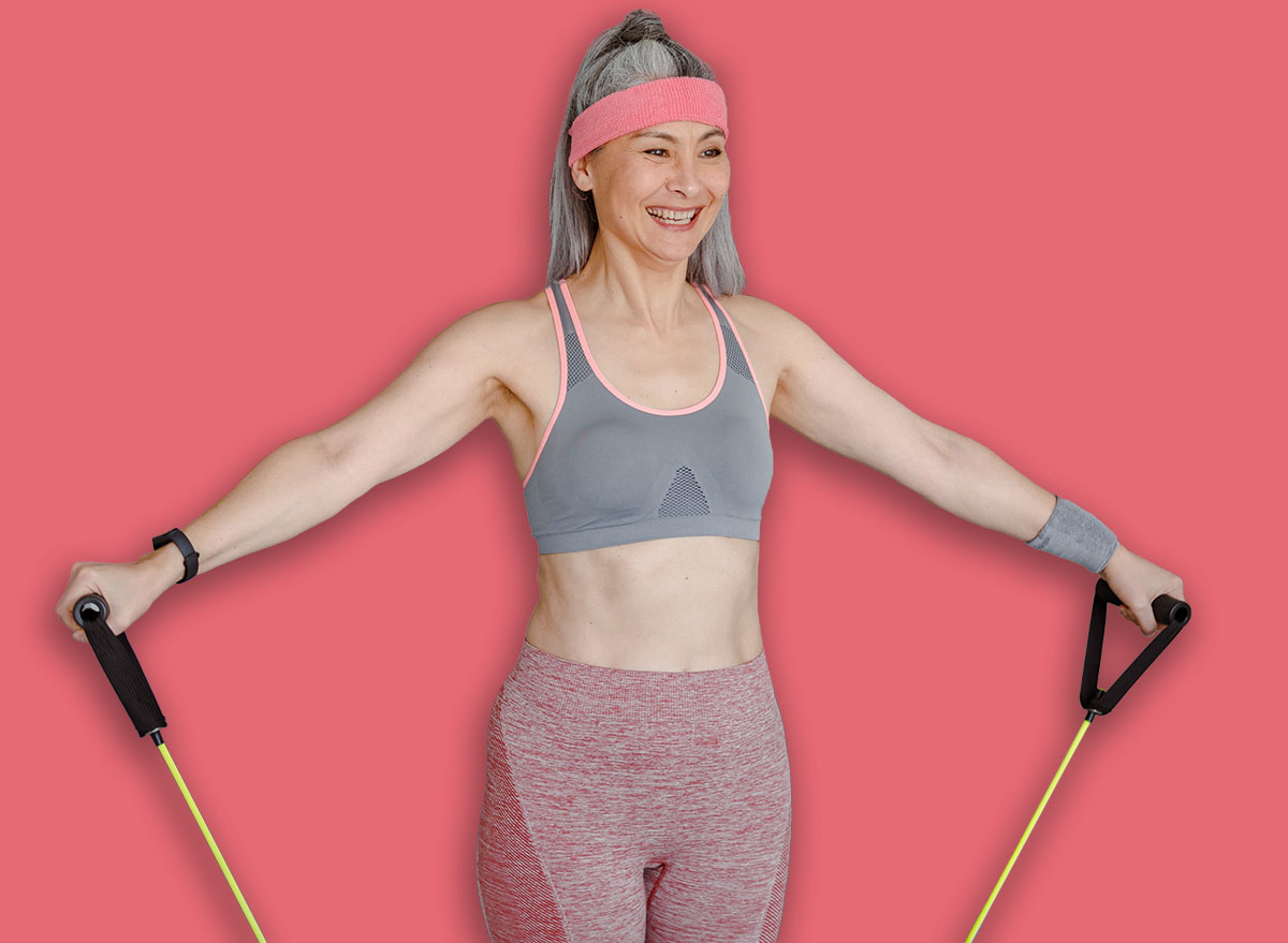 Joyful female sportswoman using resistance pull rope while having strength workout at home