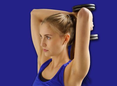 Fit young woman working out with a weight in a gym raising it behind her head with both hands to strengthen and tone her muscles in a health and fitness concept