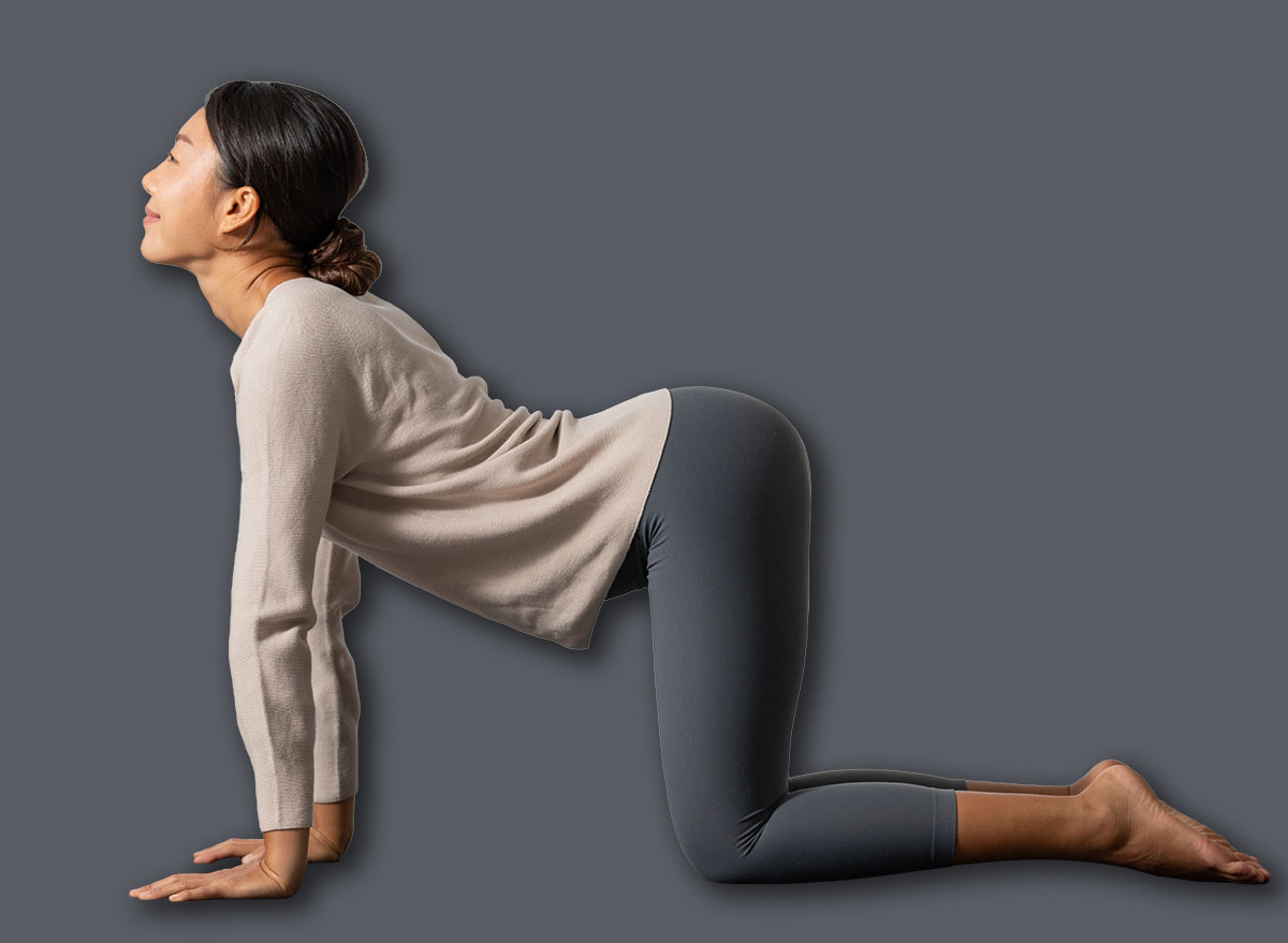 Asian young woman performing the cat-cow yoga pose on a mat in a bright, minimalist indoor setting