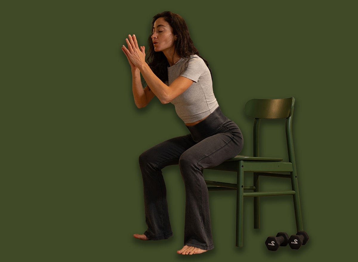 Smiling athletic woman performing chair squat exercise at home u