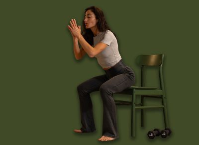 Smiling athletic woman performing chair squat exercise at home u