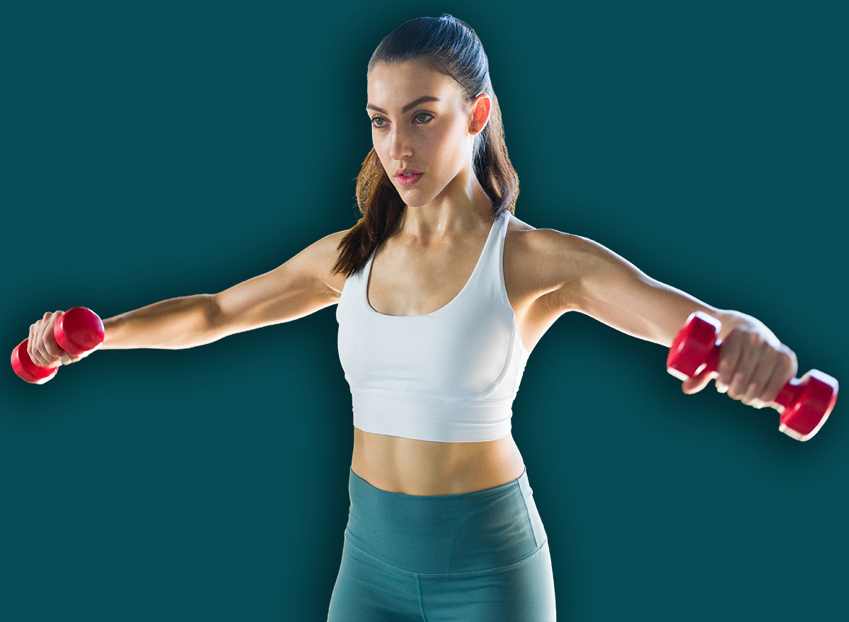 Pretty young woman with a healthy lifestyle doing side lateral raises with dumbbells indoors. Active caucasian woman exercising to stay fit and slim