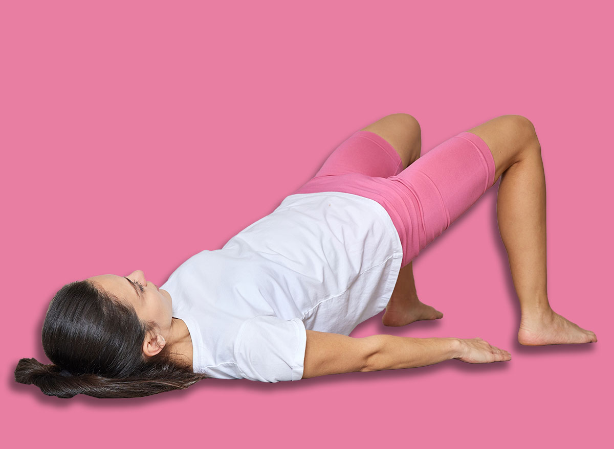 Woman performing glute bridge exercise on a yoga mat during a home workout session
