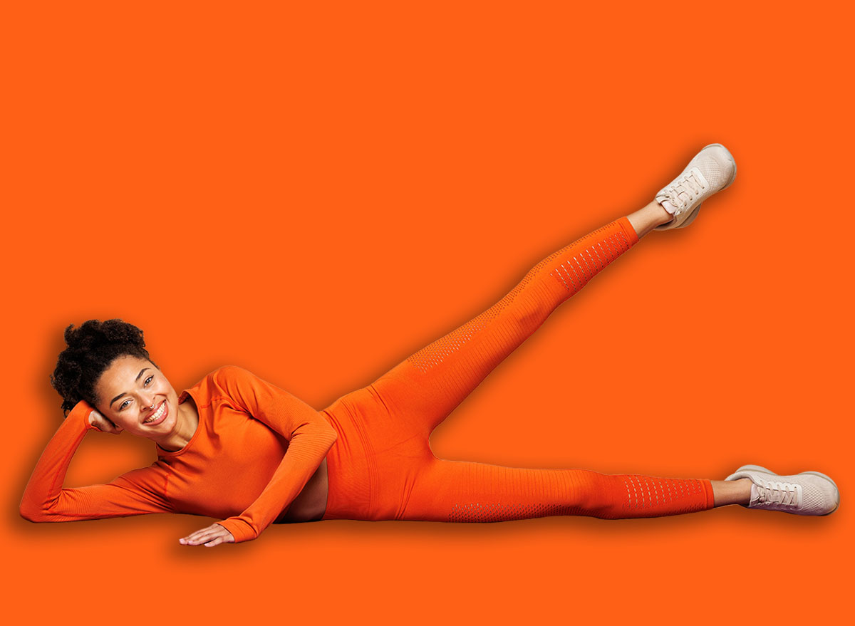 Full body young fitness trainer instructor sporty woman wear orange clothes spend time in gym do side leg raise exercise on yoga mat isolated on plain beige background. Workout sport fit abs concept
