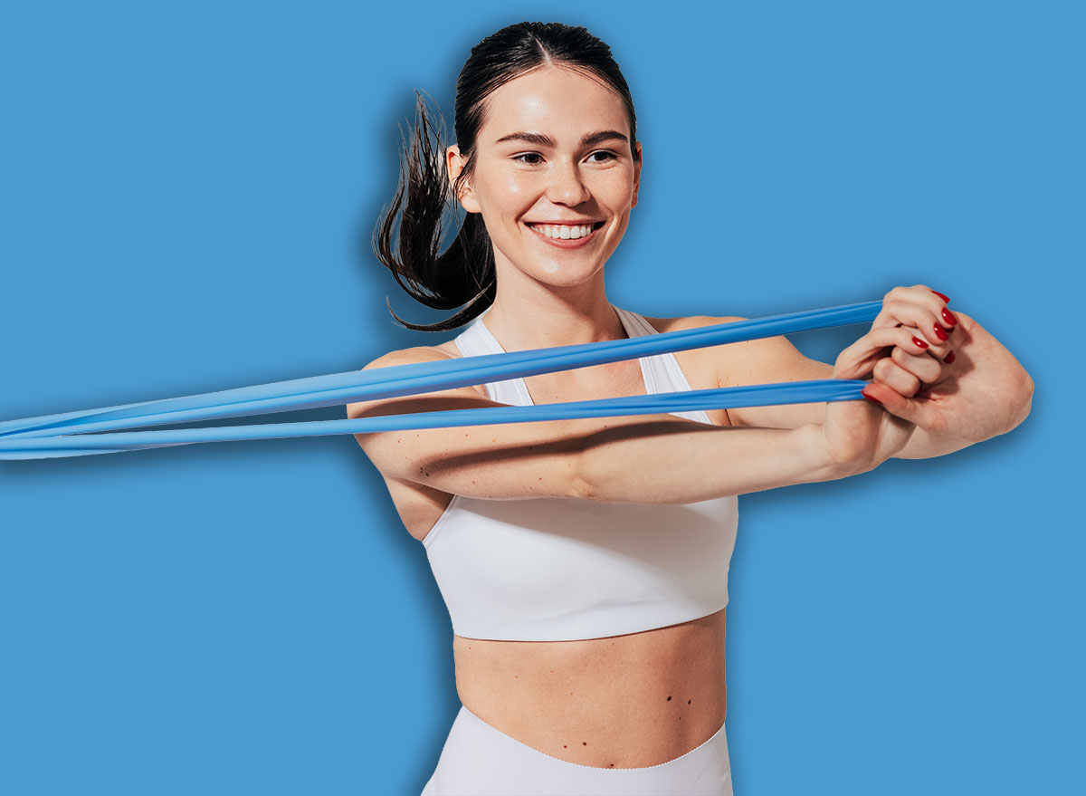 Happy sportswoman in white fitness wear pulling resistance band
