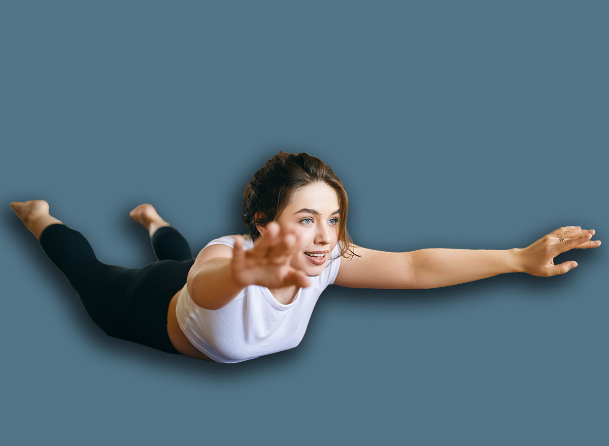 Happy energetic young woman doing yoga sequence lying face down, raising feet and extended arms, backbending for spinal strength. Healthy active lifestyle, motivation, endurance and flexibility