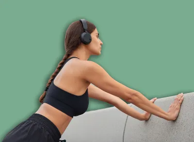 Sporty slim woman does push up exercises leans on concrrete wall wears cropped top stereo headphones on ears has pigtail poses outside has workout in open air. Motivated sportswoman in activewear