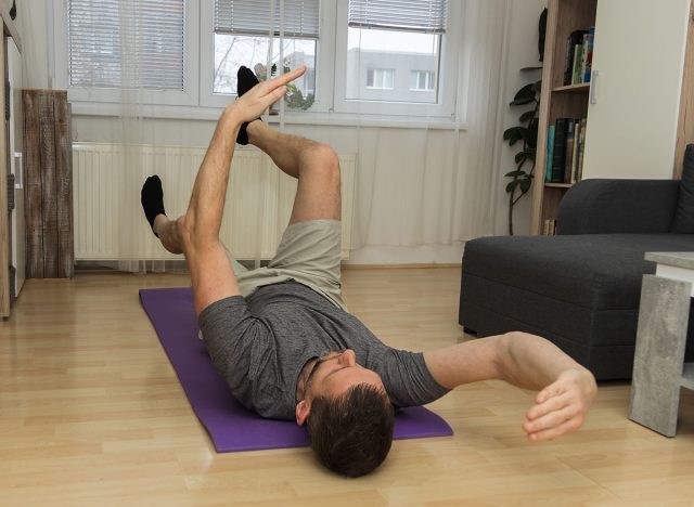 A young man does the dead bug core exercise in his living room to stabilize his spine. Healthy lifestyle, exercising at home