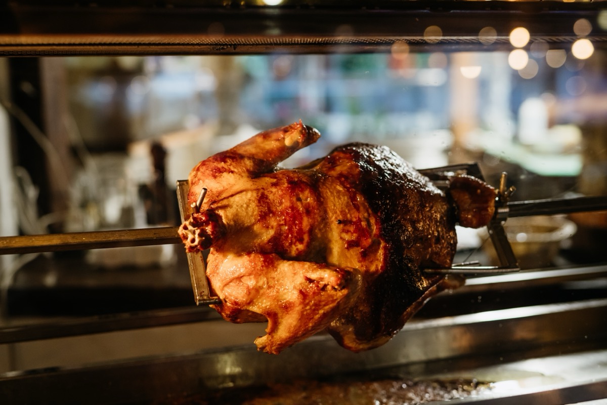 Whole roasted chicken turning on rotisserie grill.