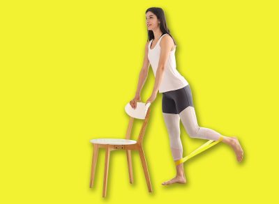 Sporty young woman with elastic band and chair training at home