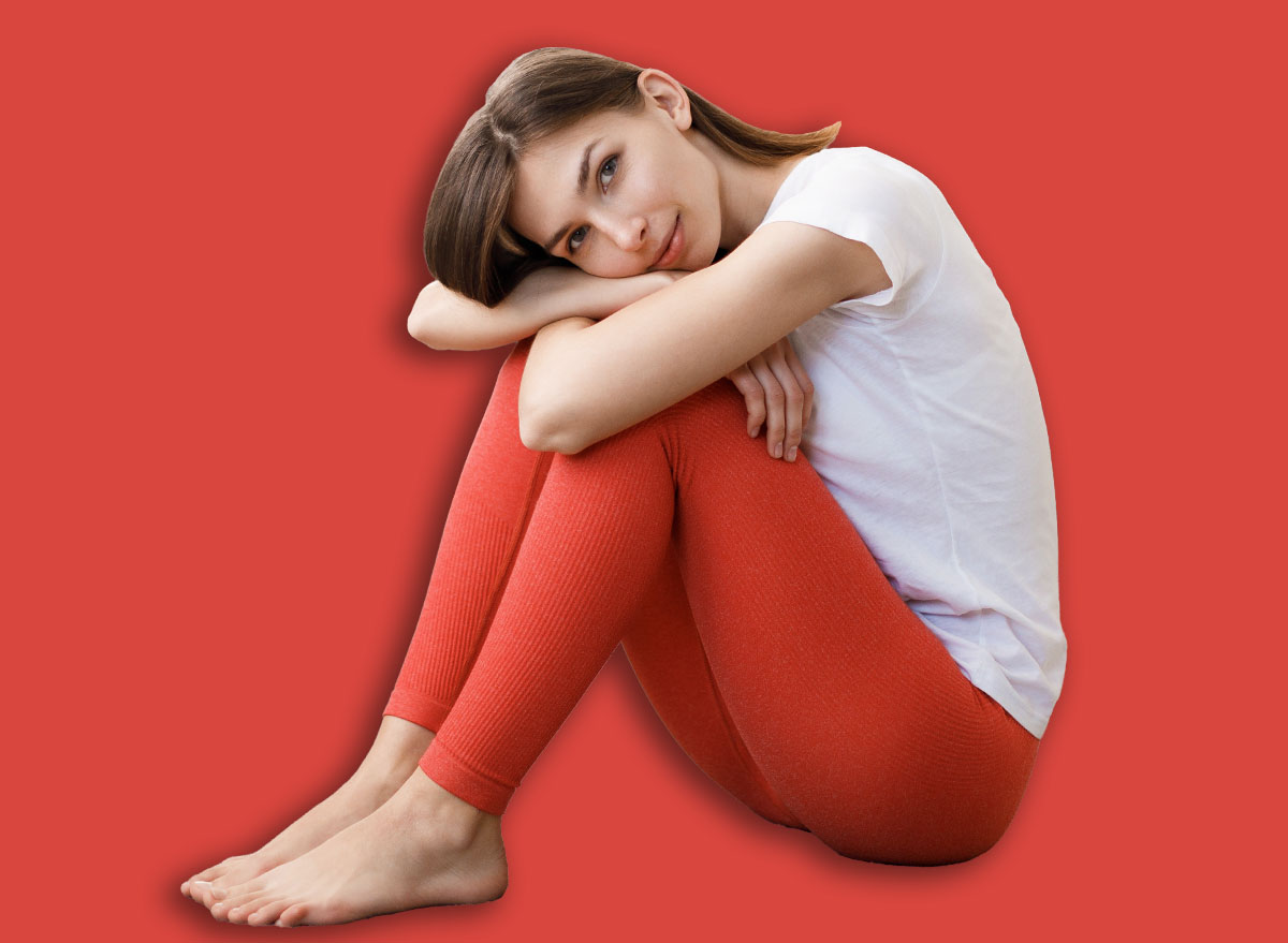 Attractive caucasian woman in sport attire leaning with head on knees while sitting on soft carpet at living room. Relaxation after domestic workout. Healthy lifestyles concept.