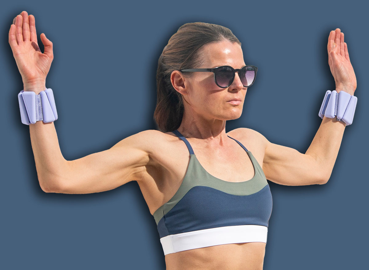 sporty woman wearing adjustable wrist weights doing a wall squat exercise with arms raised