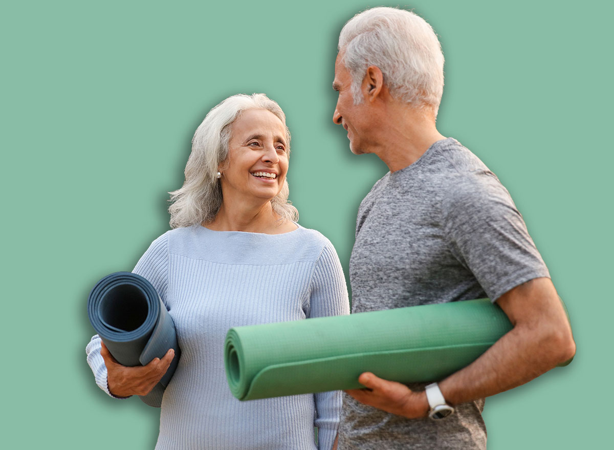 A happy old couple with gray hair happily carries yoga mats in a peaceful park setting during early morning hours.