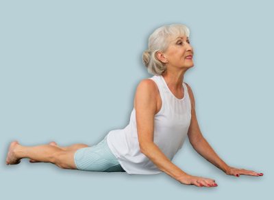 In fitness studio with small group of friends, elderly woman performs asana snake - cobra - pose dog muzzle up, Urdhva Mukha Shvanasana- Bhujangasana. Mature slender woman participates in yoga classes