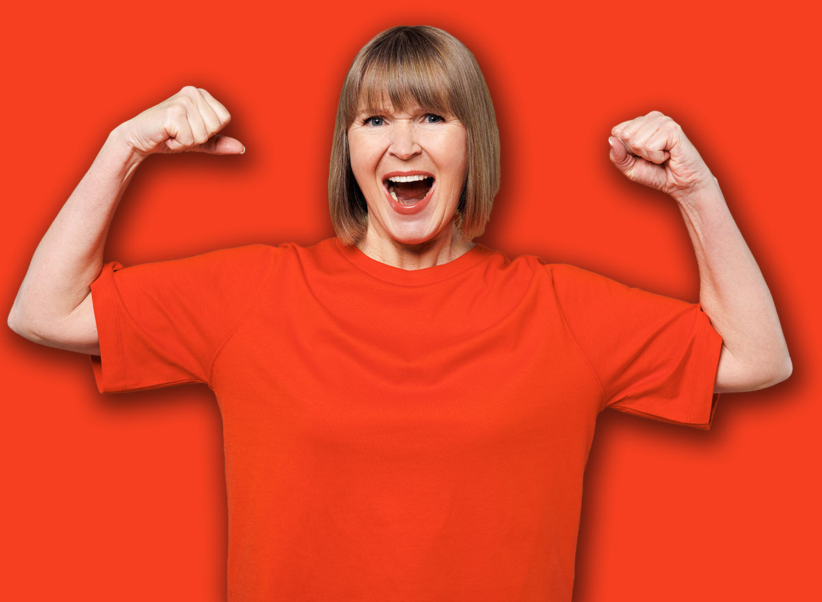 Elderly blonde woman 50s years old wear orange t-shirt casual clothes showing biceps muscles on hand demonstrating strength power isolated on plain pastel green background studio. Lifestyle concept
