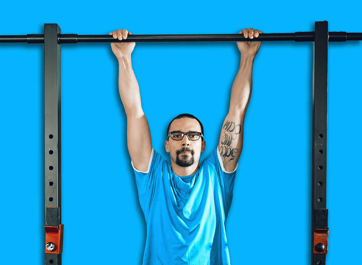 Handsome young muscular man doing pull-ups exercise at the gym. Looking at camera.