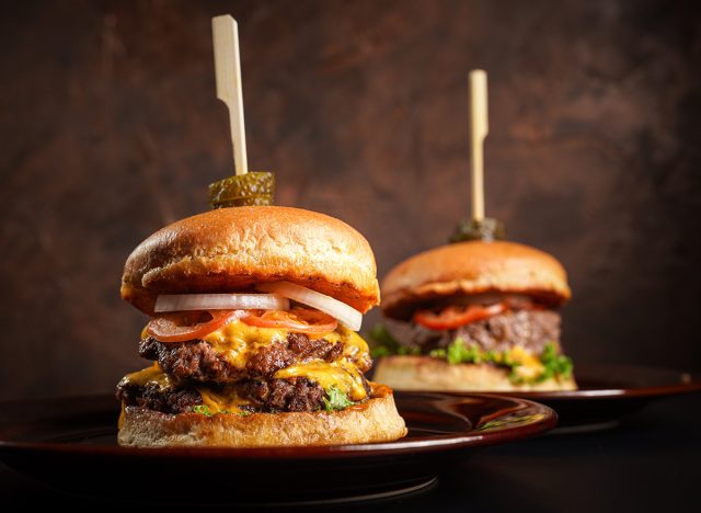 Double cheese burgers on brown dish with dark background.