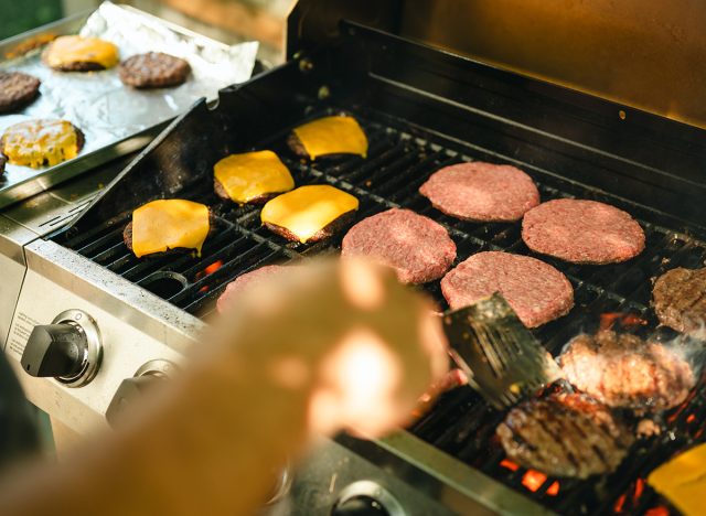 Father flipping cheeseburgers and patties grilling on outdoor barbecue