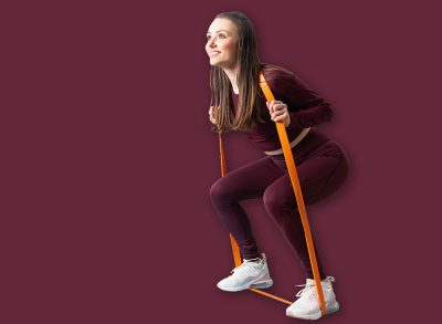 Young attractive girl squat using orange resistance band on blue exercise mat. Home booty workout.