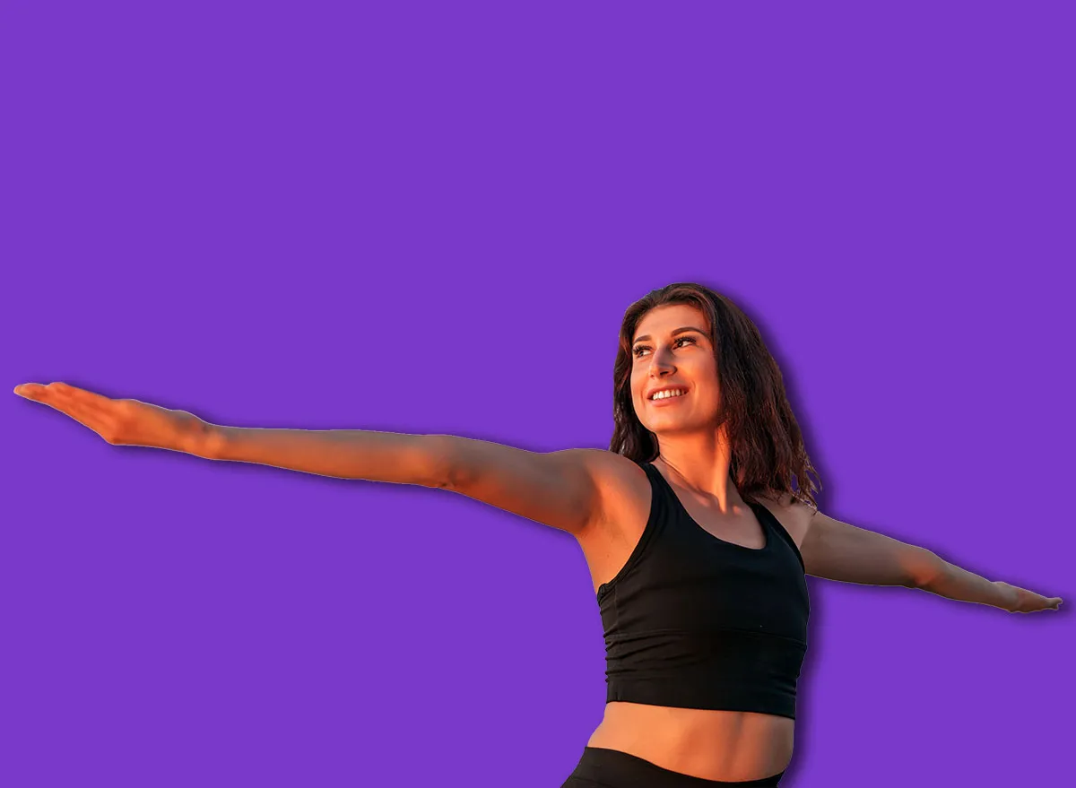 Smiling sportswoman practicing yoga on the beach at sunset, arms outstretched and embracing the serene beauty of the ocean