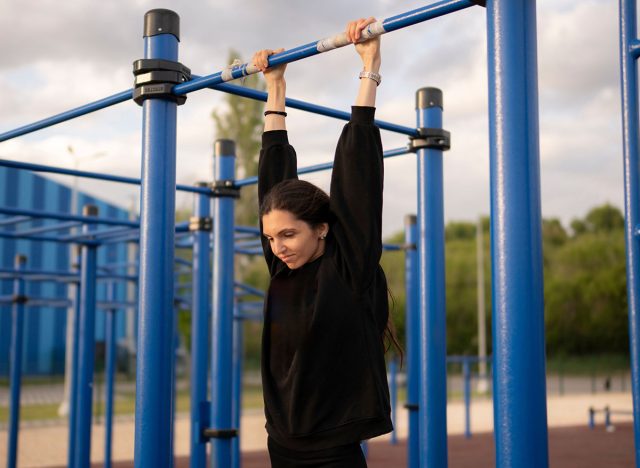 Young Female Athlete Hanging on the Bar on Outdoor Exercise Equipment