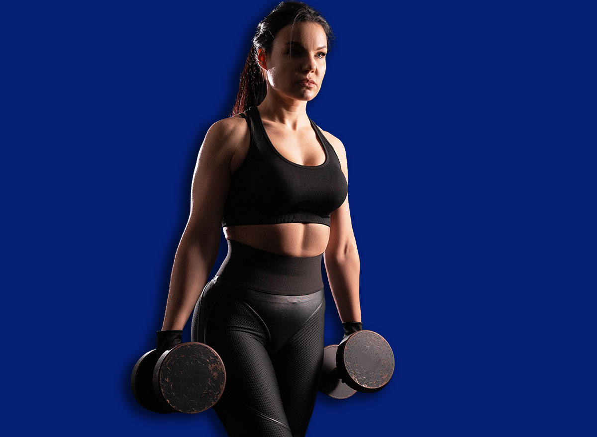 Determined woman loses weight in the gym and trains with dumbbells. The concept of sports and recreation. Beautiful woman in sportswear with heavy dumbbells in her hands.