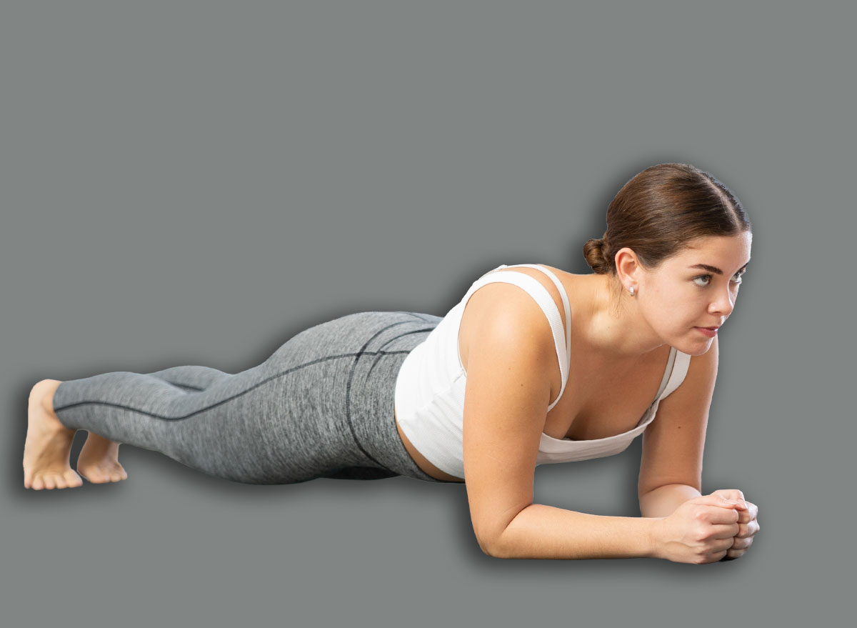 Attractive fit young woman holding forearms plank pose, Phalakasana asana, to strengthen abs muscles during group training in yoga studio. Active lifestyle concept ..