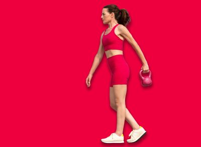Sporty mid adult woman carrying a kettlebell weight, training outdoors. Red sports clothing.