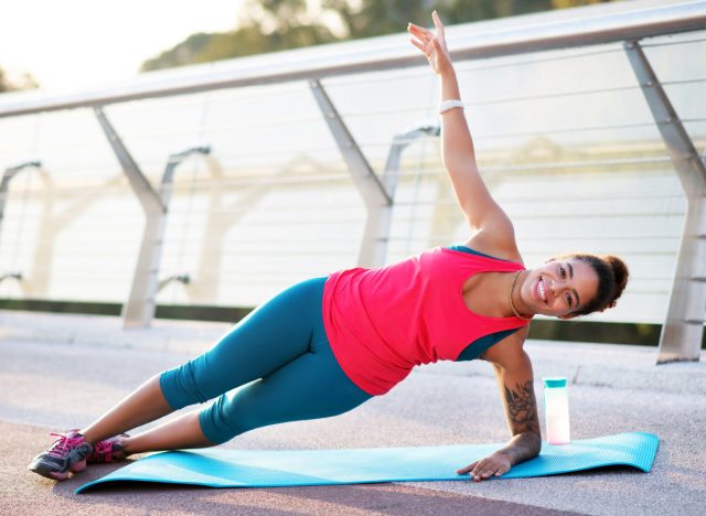 Doing side plank. Smiling African-American woman doing side plank while finishing workout