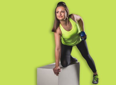 A woman in neon activewear executes a dumbbell row while kneeling on a white box, showcasing strength, focus, and proper form in a professional studio setting