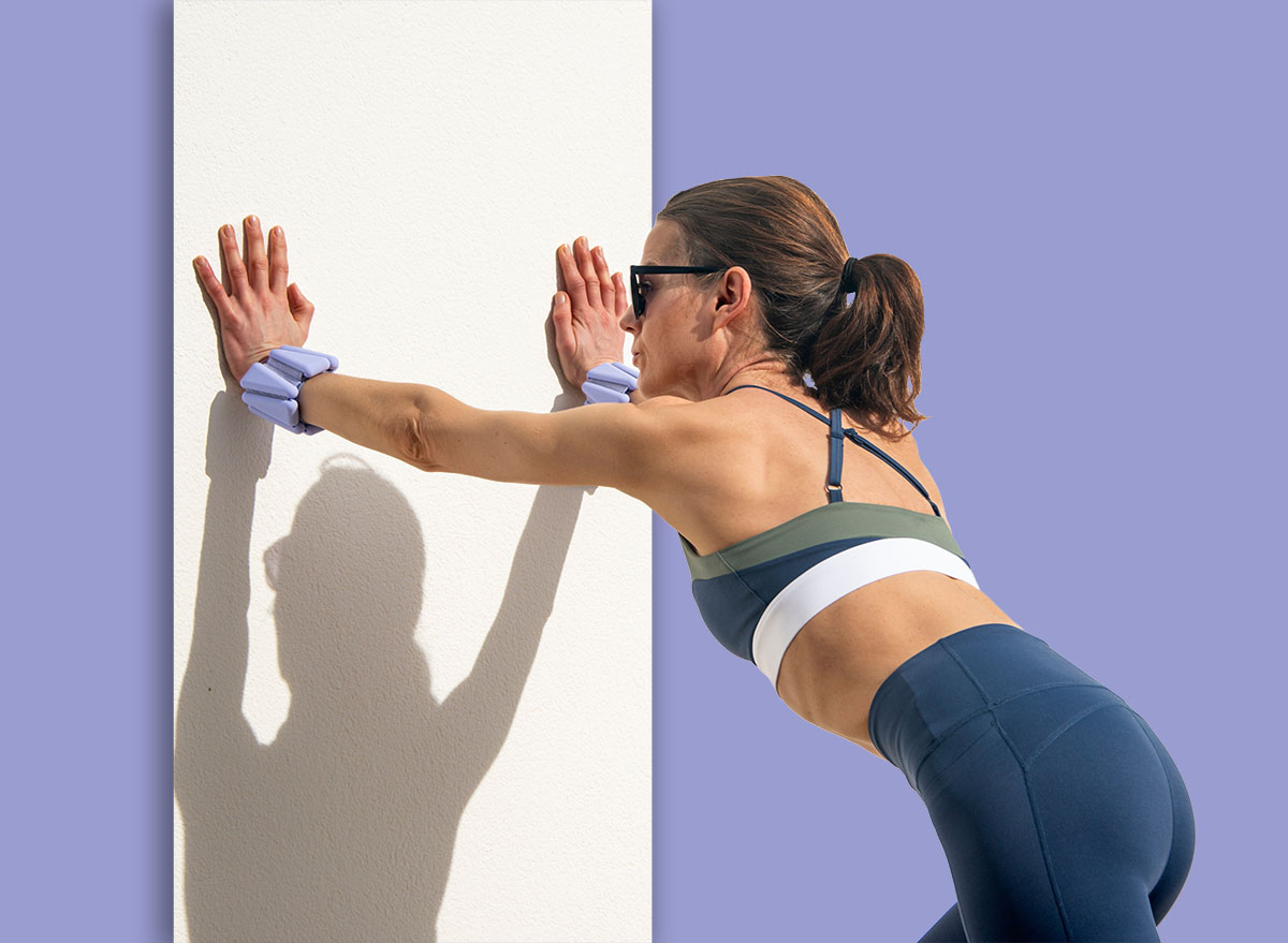 sporty woman wearing sports clothing wearing adjustable wrist weights doing push off exercise against a white wall