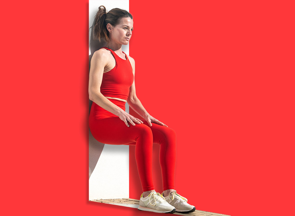 Athletic female performing wall squat exercise outdoors against white wall