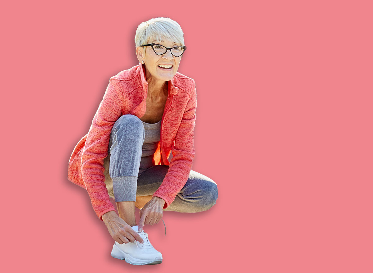Portrait of a happy active beautiful senior woman posing fixing shoelace on her running shoe after exercising outdoors