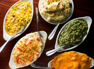 Steakhouse side dishes. Asparagus, salad, tomatoes, mashed potatoes, red onions, cream cauliflower, pickled peppers, seasoned meats served in cast iron skillet. Traditional appetizer items.
