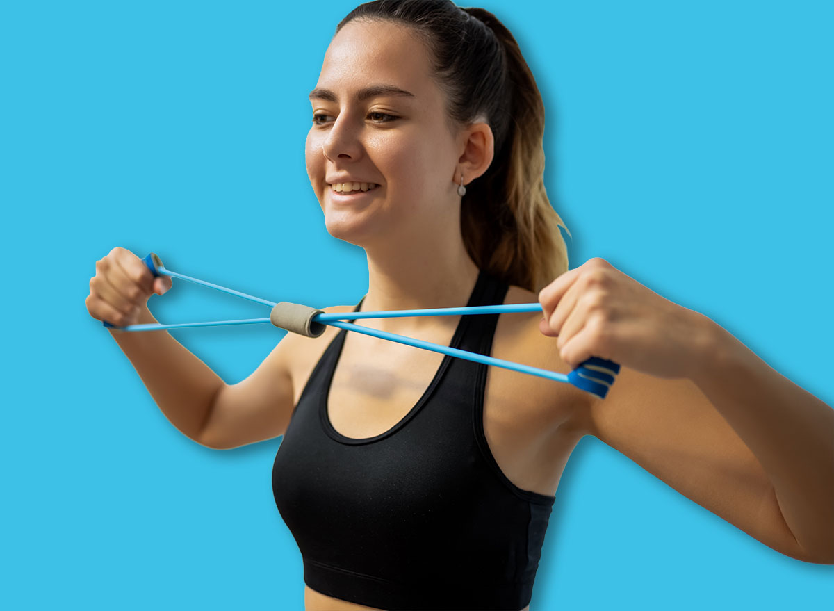 A female athlete in activewear sitting , pulling an elastic band with bent elbows to strengthen her upper back and shoulder blades. Focus on home fitness and back health.