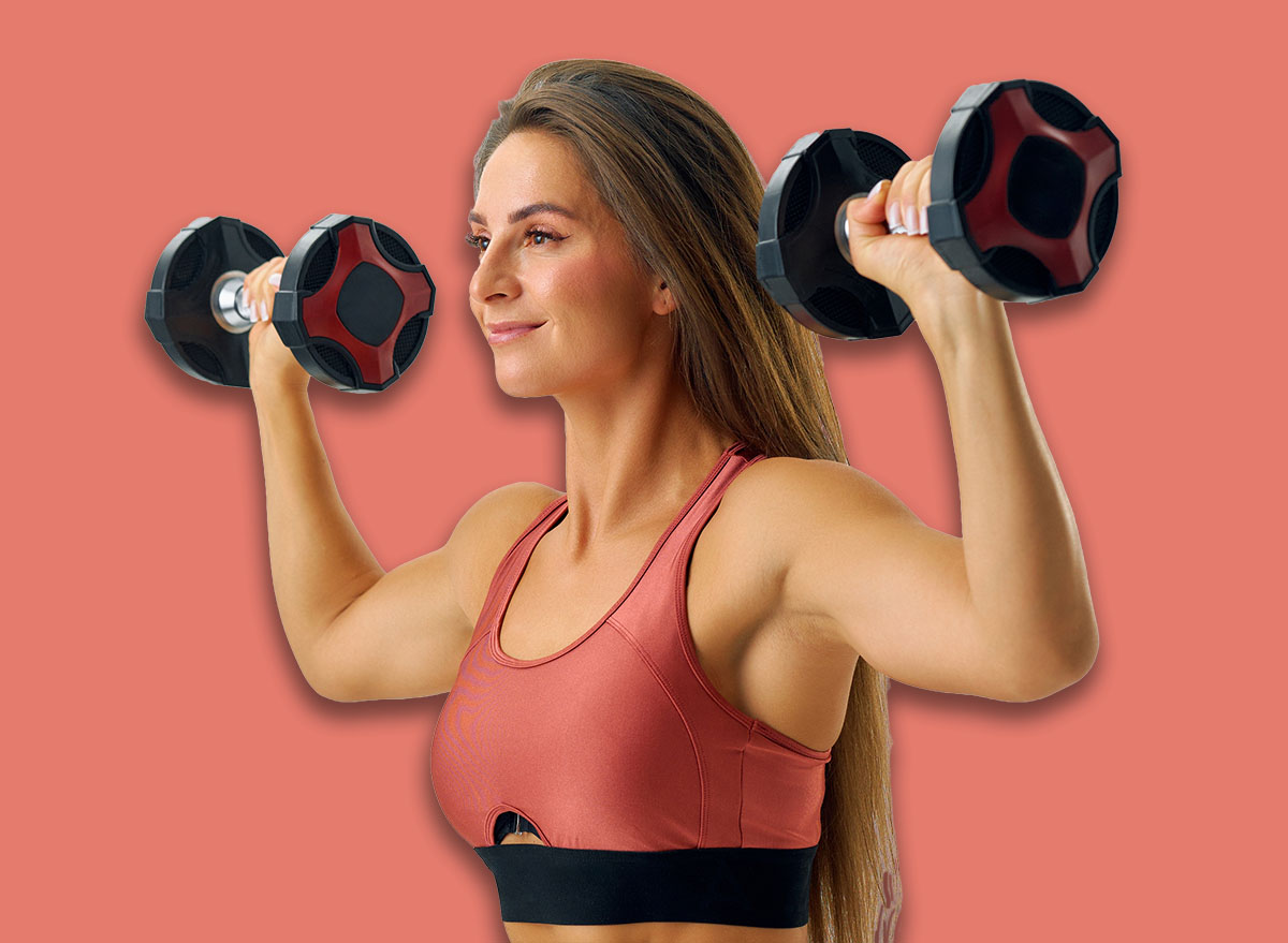 White studio, a sporty woman confidently executes an overhead press with a pair of dumbbells.