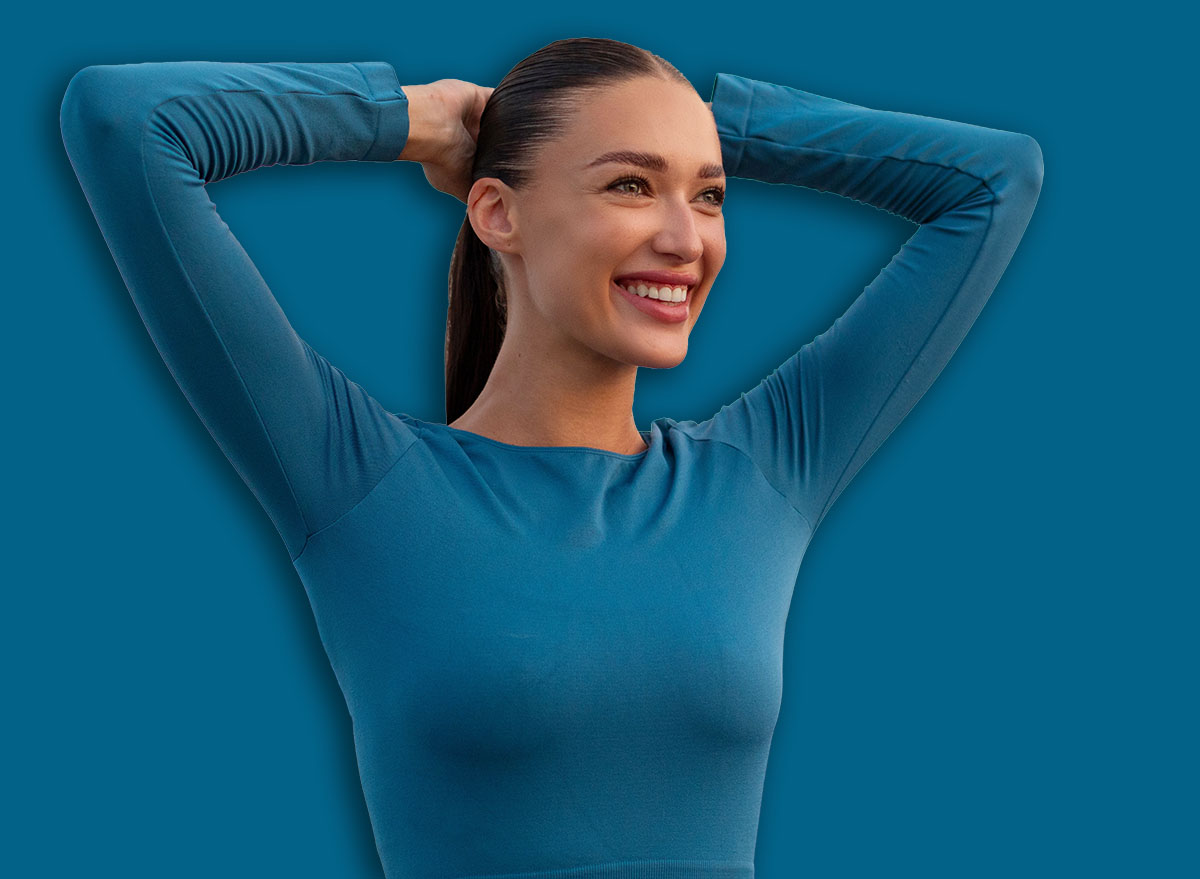Attractive young European woman doing stretching gymnastic exercises before running, warming up and smiling, standing on bridge in the evening