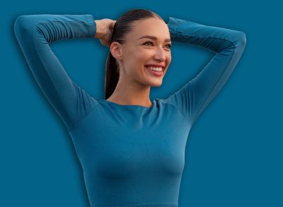 Attractive young European woman doing stretching gymnastic exercises before running, warming up and smiling, standing on bridge in the evening