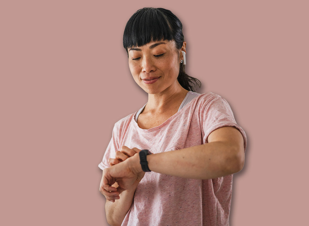 Healthy fit japanese woman training at home on exercise static bike during workout looking at smart watch coaching app for motivation. Successful female health weekly habits