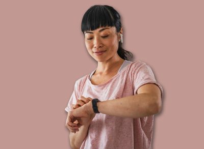 Healthy fit japanese woman training at home on exercise static bike during workout looking at smart watch coaching app for motivation. Successful female health weekly habits