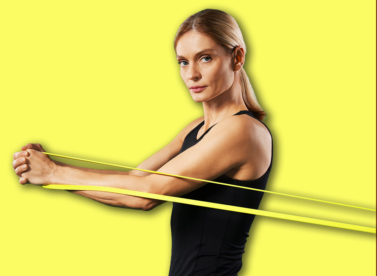 Athletic woman exercising with elastic resistance band on green background