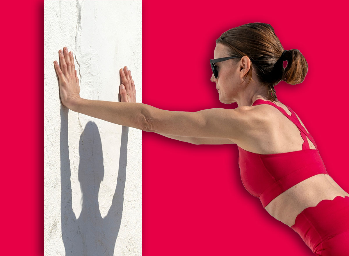 fit woman in red activewear doing push off exercise against a white wall outdoors