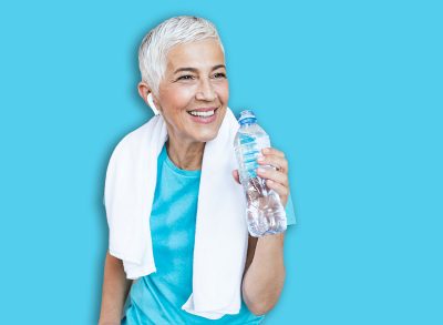 Elderly woman sitting on the sofa, exhausted after the daily training.Senior woman taking a break while exercising at home. Athletic mature woman holding bottle of water,Having a towel around her neck