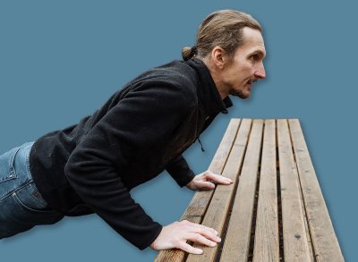 athletic man doing incline pushups in park, person executing incline pushups with park equipment nearby, individual engaging in incline pushups on wooden bench at outdoor fitness park
