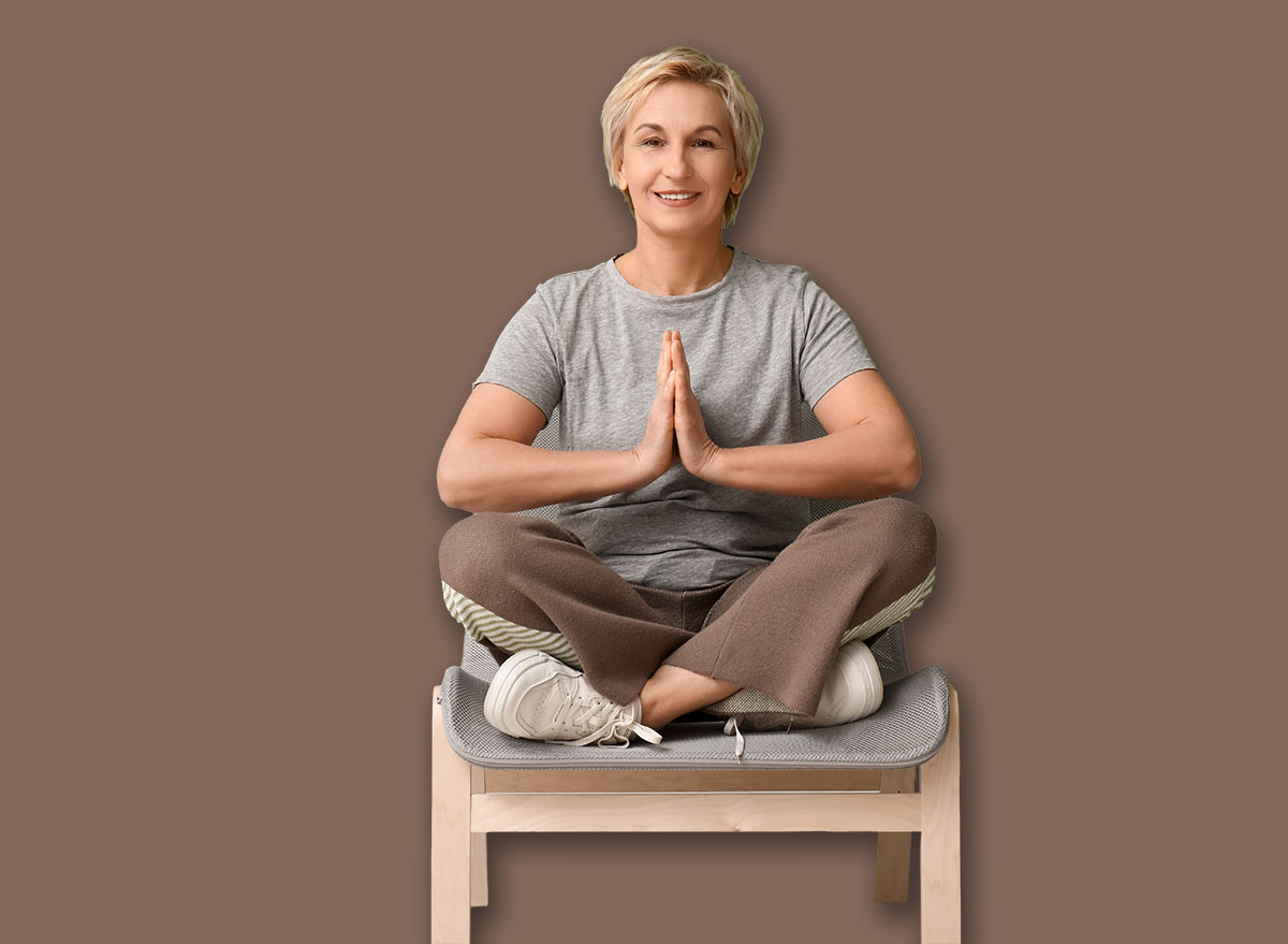Portrait of meditating mature woman sitting on chair against green wall