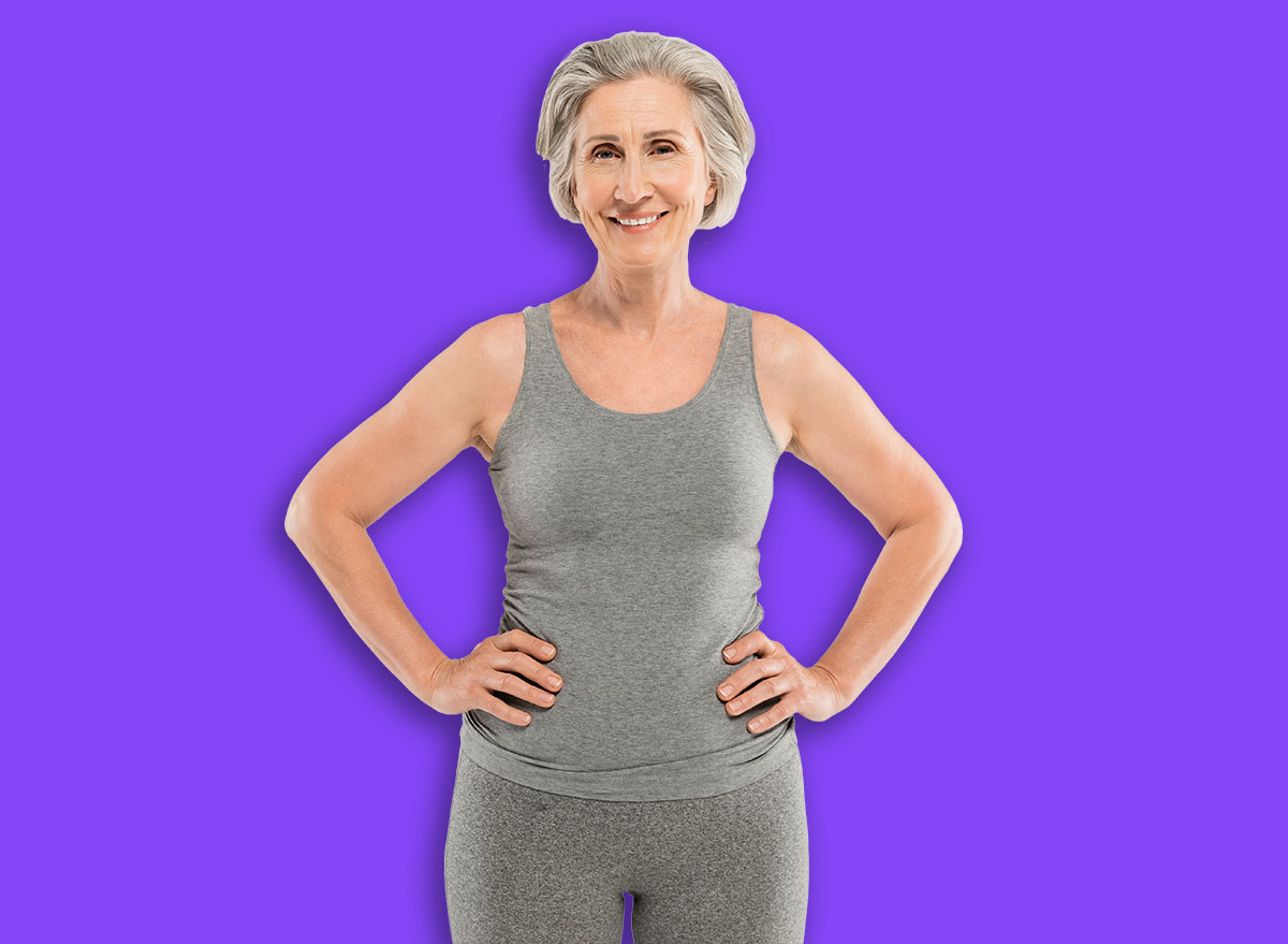 happy senior woman in tank top standing with hands on hips isolated on grey