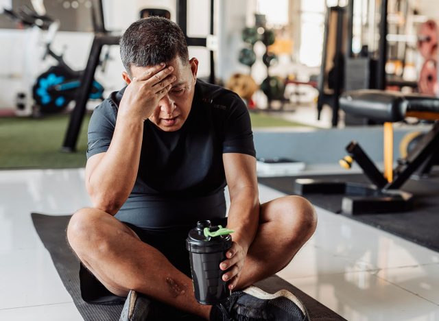 Southeast Asian man in his 50s shows disappointment after an intense workout, sitting exhausted on mat with hand on forehead.
